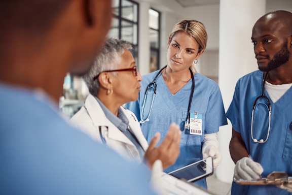 A group of medical professionals in blue scrubs are gathered around a patient.