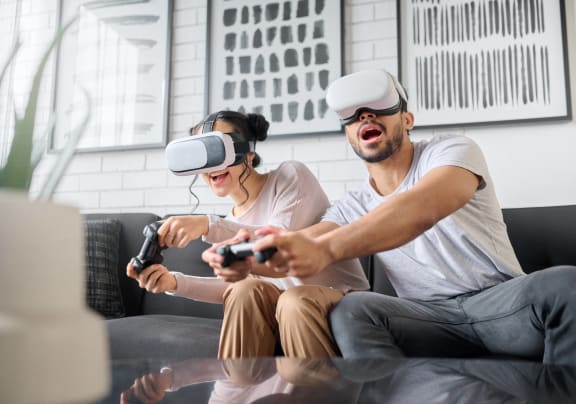 a man and woman sitting on a couch playing video games with virtual reality goggles on at Altis Santa Barbara, Florida