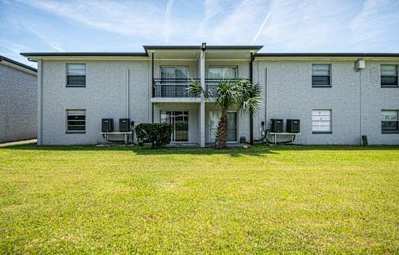 the front of a white house with a yard and a palm tree at Palm Cove Apartments, Daytona Beach Florida