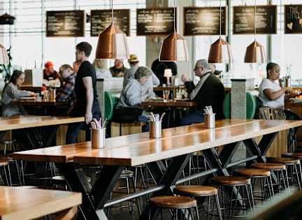 A group of people are sitting and standing around wooden tables in a restaurant.