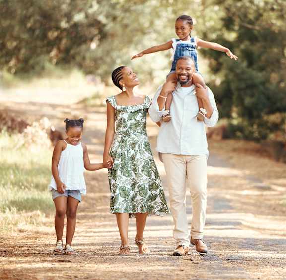 A family of four is walking down a dirt road holding hands.