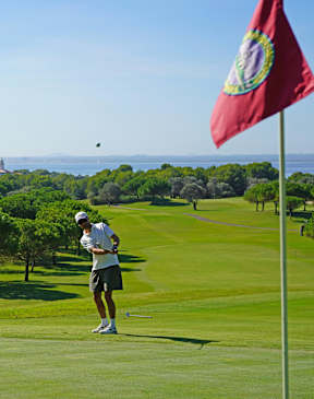 A golfer is on a golf course with a red flag in the background.