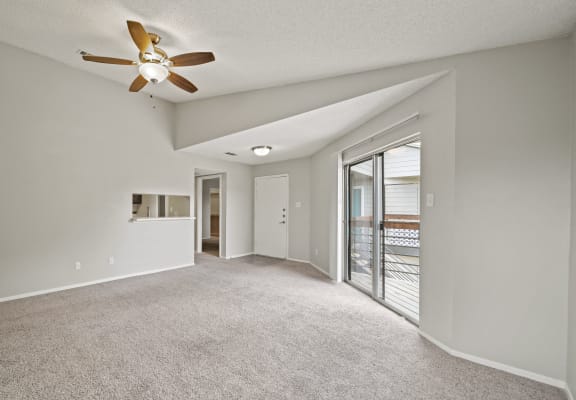 an empty living room with a ceiling fan and a door to a balcony