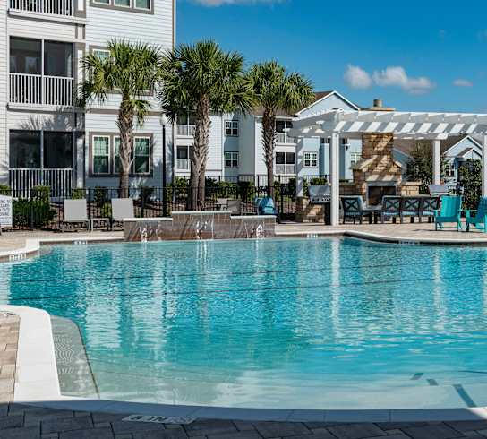 a large swimming pool with blue chairs and a white pergola in the background