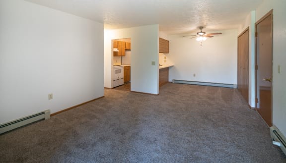 an empty living room with a ceiling fan and a kitchen