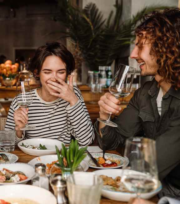 Three people are sitting at a table with plates of food and glasses of wine.