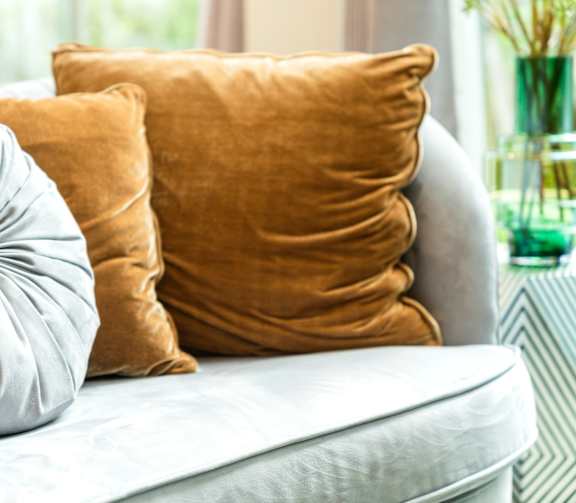 A grey couch with a white and a mustard yellow pillow on it.