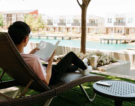 A person is reading a book on a chair by a pool.