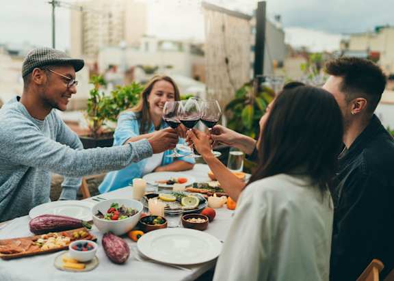 A group of people toasting with wine glasses at a table full of food.