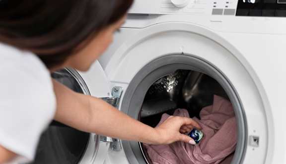 A woman is loading a pink shirt into a washing machine.