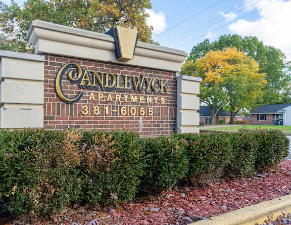 A sign for Candlewick Apartments with a brick background and a black and white striped awning.