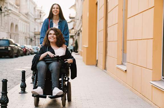 a woman pushing a woman in a wheelchair down a street