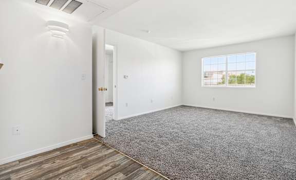 an empty room with white walls and wood flooring and a window