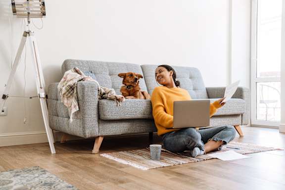 A person is sitting on a brown couch writing in a notebook.