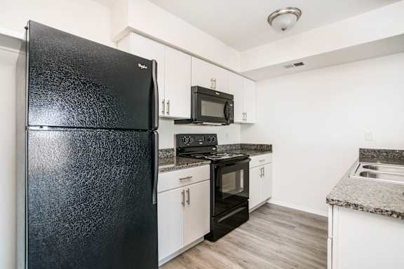 A black fridge in a kitchen with white cabinets.
