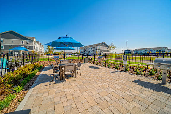 A patio with a table and chairs and umbrellas in front of apartment buildings.