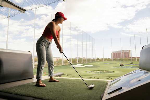 A woman in a red cap and red top is playing golf.