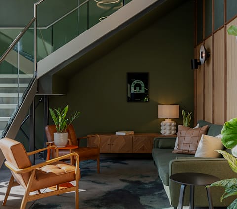 A living room with a green couch, a wooden chair, and a glass staircase.