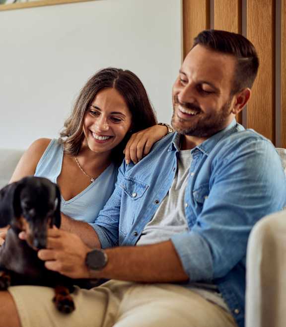 A man and woman are sitting on a couch with a dog between them.