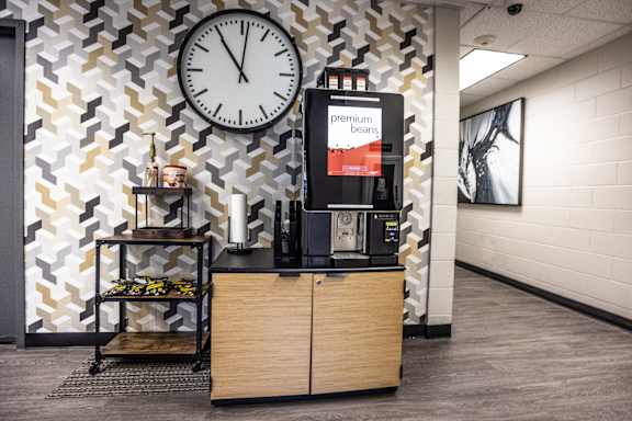 A coffee machine is on a counter in a room with a clock on the wall.