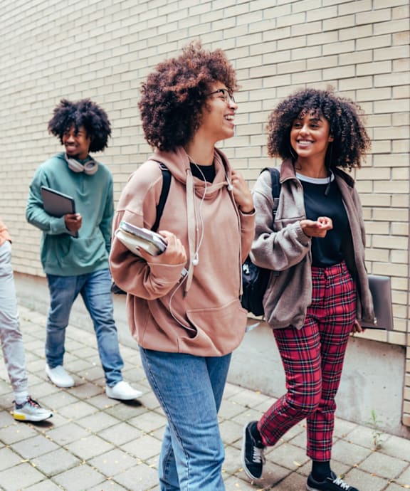Three people walking on a sidewalk, one of them holding a book.