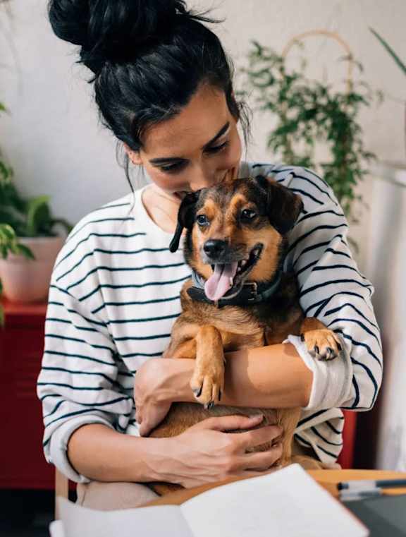 A woman in a striped shirt is holding a happy dog.