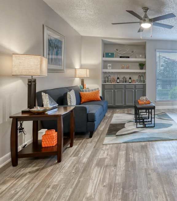 A living room with a grey sofa, a wooden table, and a ceiling fan.