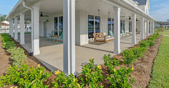 the front porch of a white house with columns and a porch swing