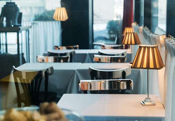 A restaurant with tables and chairs and a view of the street outside.