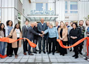 Thumbnail 1 of 24 - A group of people are gathered for a ribbon cutting ceremony outside of a building with a sign that says "St. Luke's".