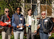 Thumbnail 10 of 24 - Four people are standing outside holding drinks and papers.