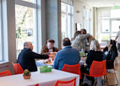 Thumbnail 12 of 24 - A group of people hug each other in a room with red chairs.