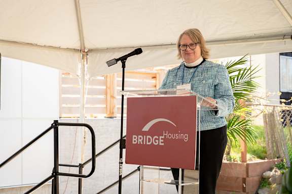 A woman stands behind a podium with a sign that says Bridge Housing.
