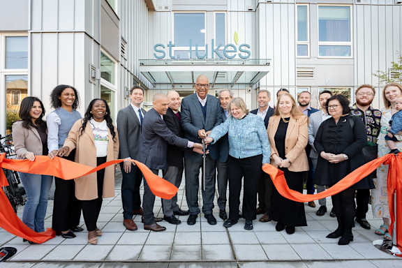 A group of people are gathered for a ribbon cutting ceremony outside of a building with a sign that says "St. Luke's".