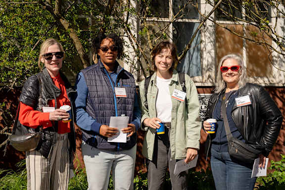 Four people are standing outside holding drinks and papers.