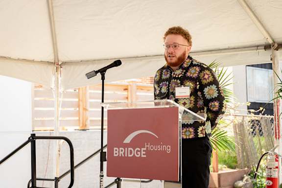 A man is giving a speech at a podium with a sign that says BRIDGE Housing.
