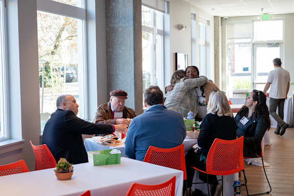 A group of people hug each other in a room with red chairs.
