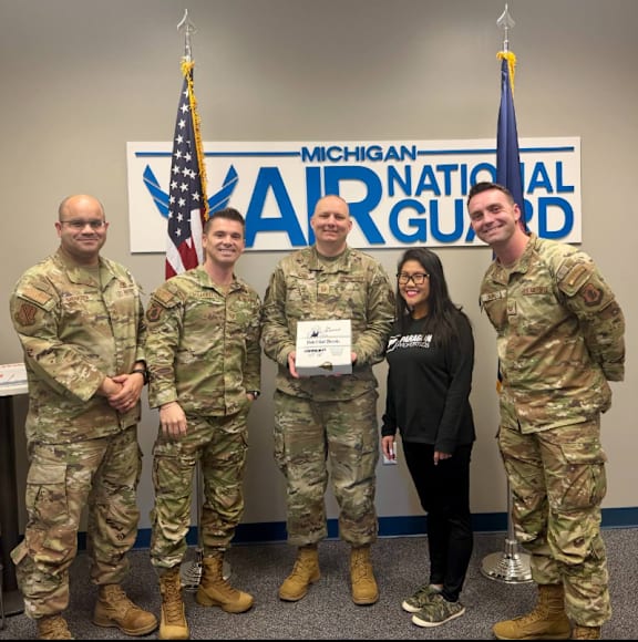 A group of people in military uniforms stand in front of a sign that says "Michigan National Guard".