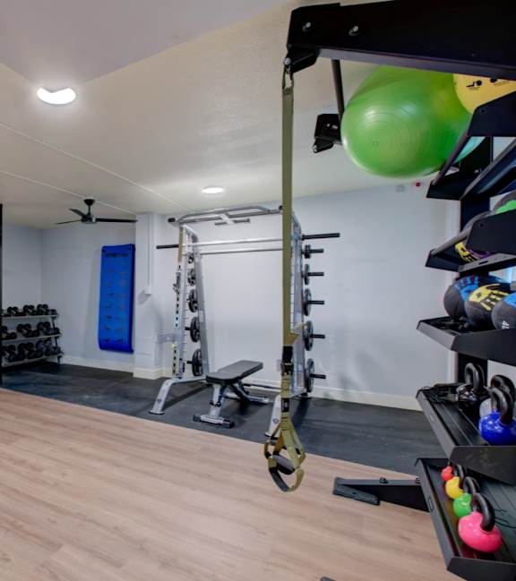 A gym with a weight rack, a bench, and a fan.