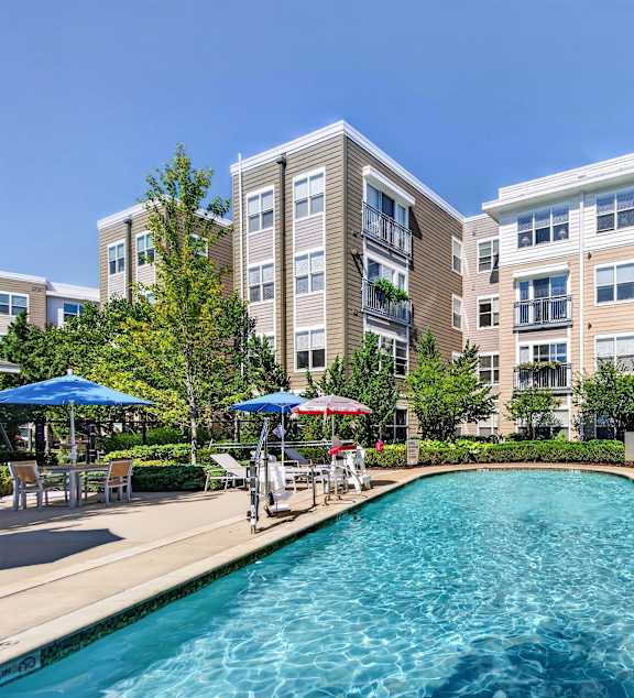 A large swimming pool in front of apartment buildings with blue umbrellas.