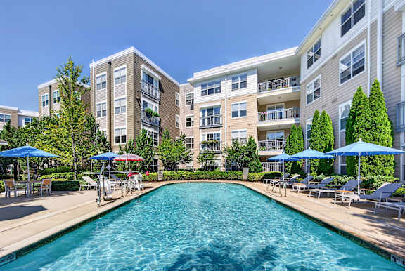 A large swimming pool in front of apartment buildings with blue umbrellas.