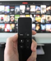 a hand holding a remote control in front of a television