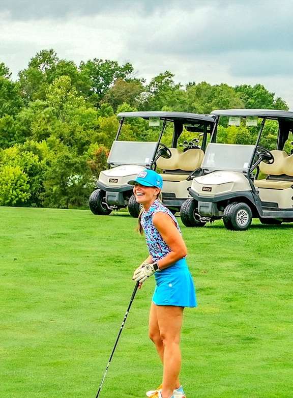 A woman in a blue top and skirt is playing golf on a sunny day. at Northlake Park Apartments, Orlando, FL