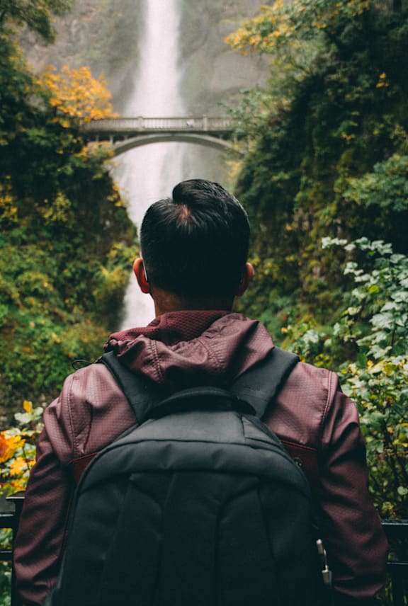 Man Wearing Backpack and Admiring Waterfall