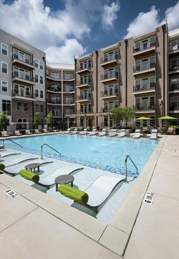 a large swimming pool with chaise lounge chairs in front of an apartment building