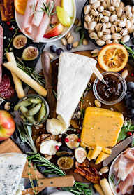 A variety of cheeses, meats, fruits, and nuts are arranged on a wooden board for a charcuterie board.