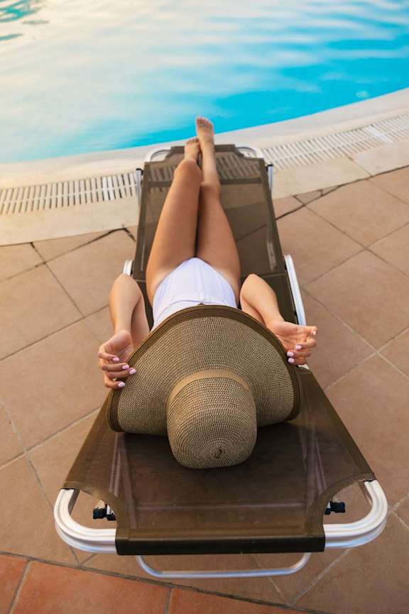Resident relaxing on a lounge chair beside a resort-style swimming pool with clear blue water and sunlit deck at an apartment community.