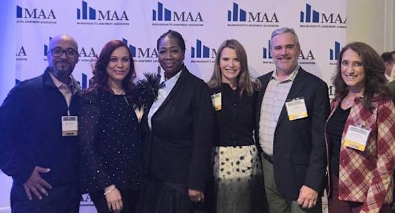 A group of people are standing in front of a backdrop with the letters "MAA" on it.