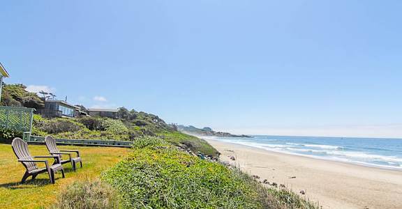 A beach scene with chairs and a house on the hillside.