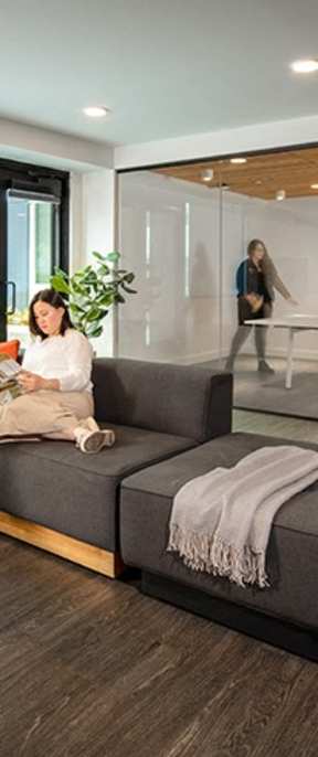 A woman is sitting on a grey couch in a modern living room.